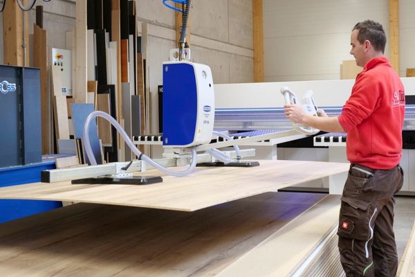 Ein Mann hebt mit Hilfe eines Lastenhebesystems eine große Holzplatte an.